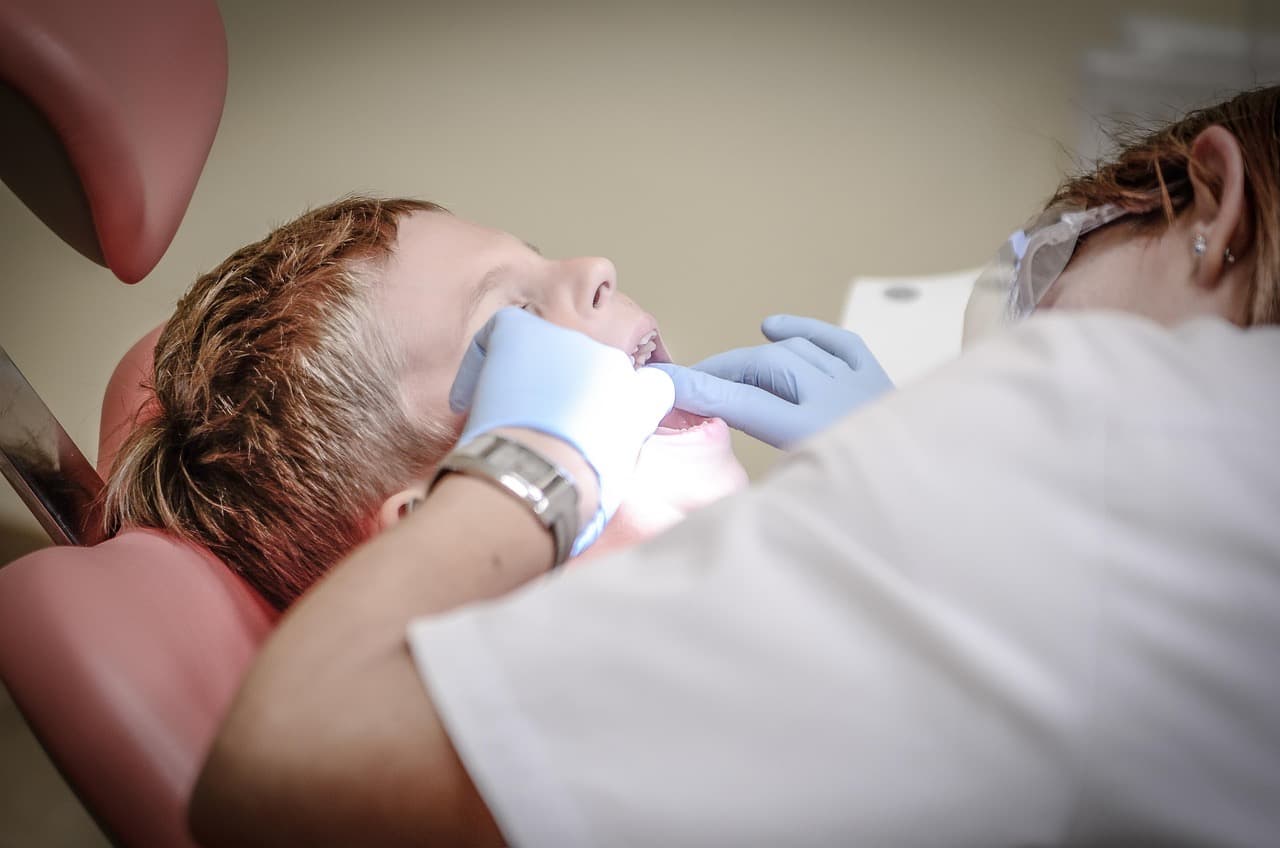 A dentist examining a patient's mouth while the patient lies in the treatment chair