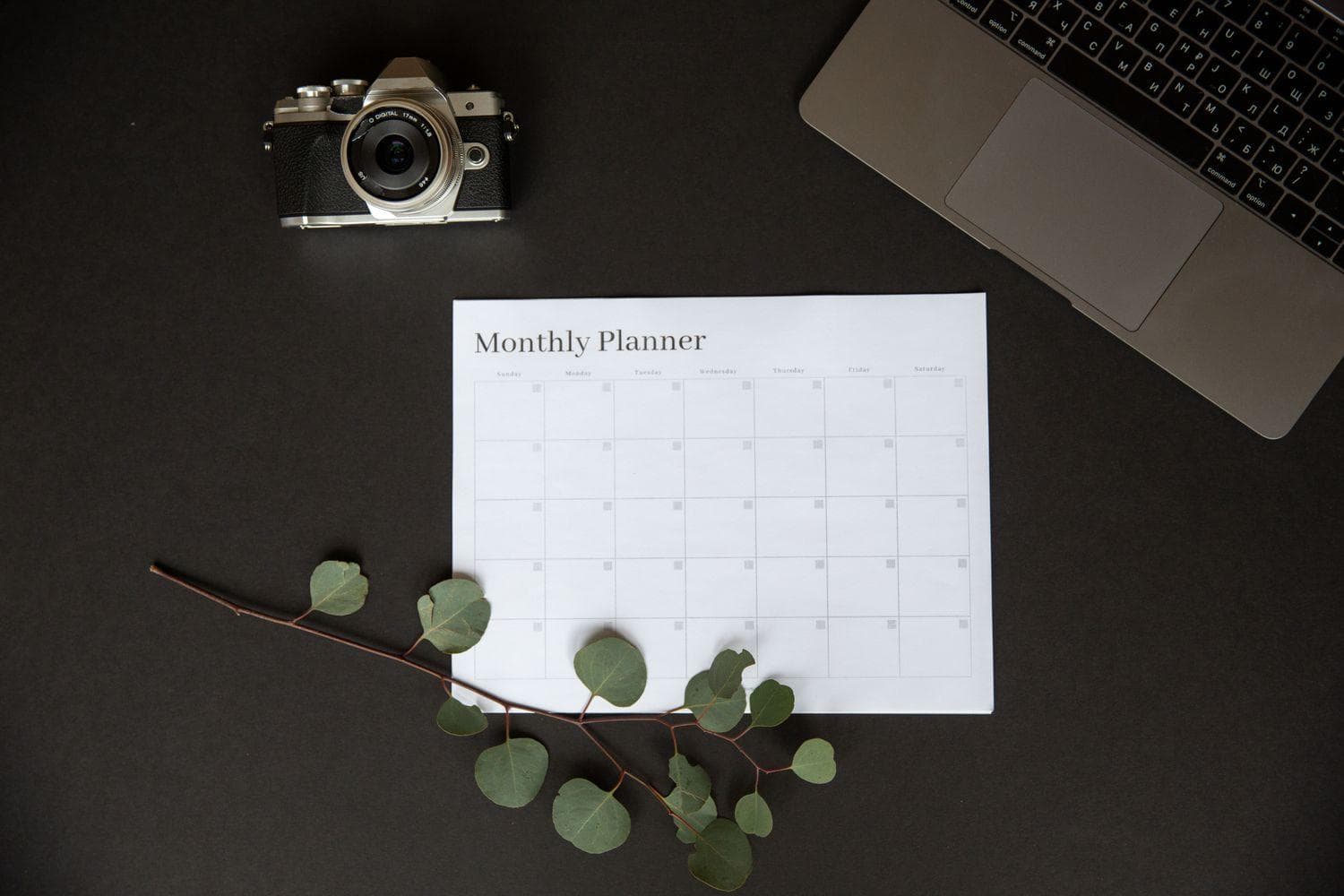 A camera, laptop, and monthly content calendar laid out on a dark desk