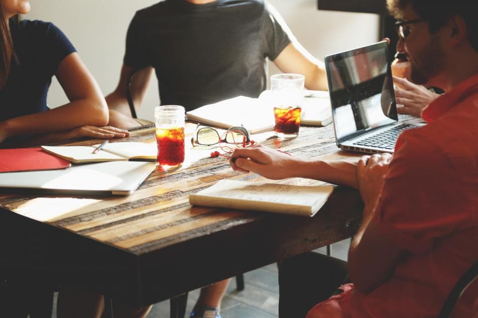 A team of three working with laptops and notebooks around a wooden table