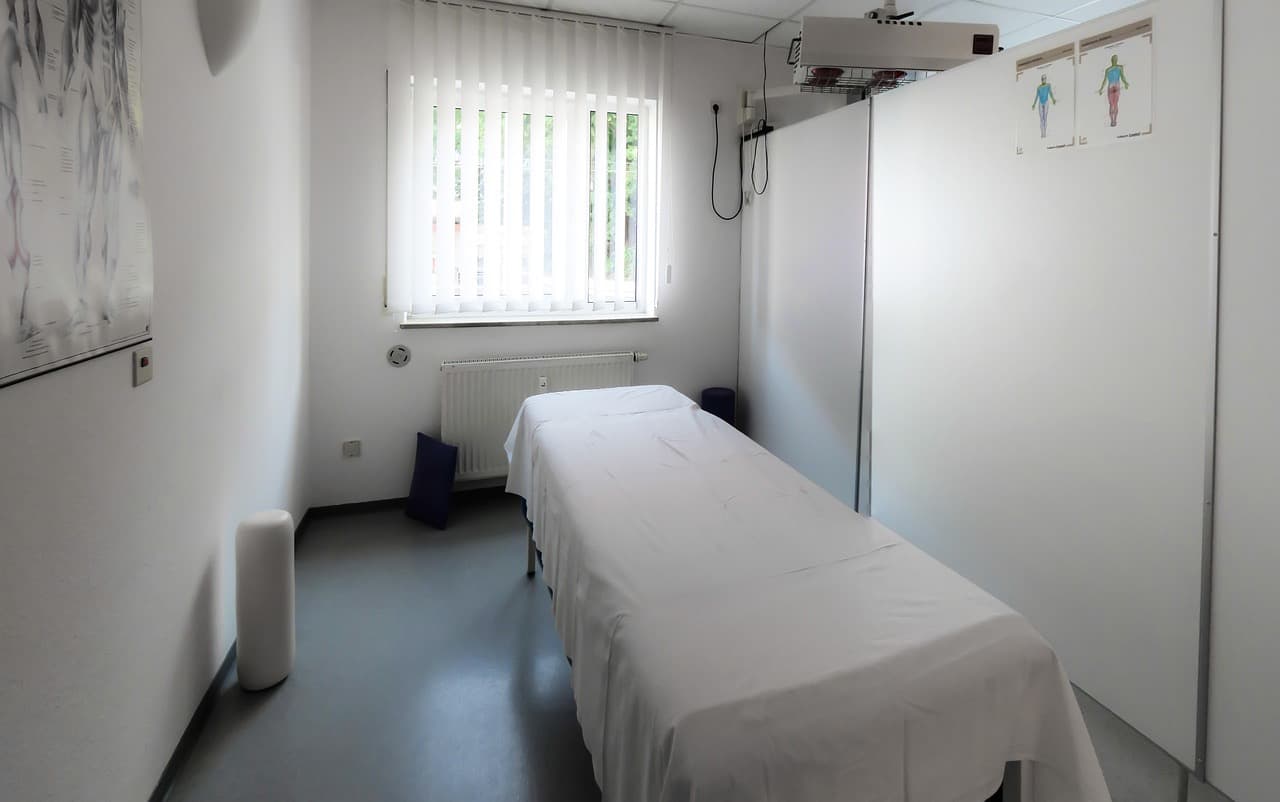 A simple physiotherapy treatment room with a treatment table, anatomy poster, and infrared lamp