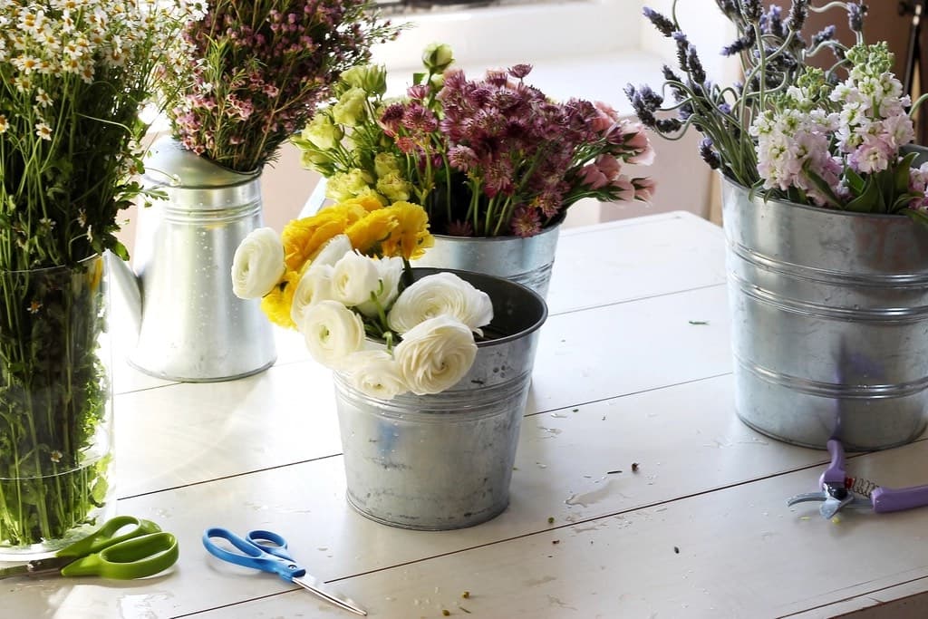 Flower bouquets in metal buckets on a white table with scissors and pruning shears beside them — a small local flower shop